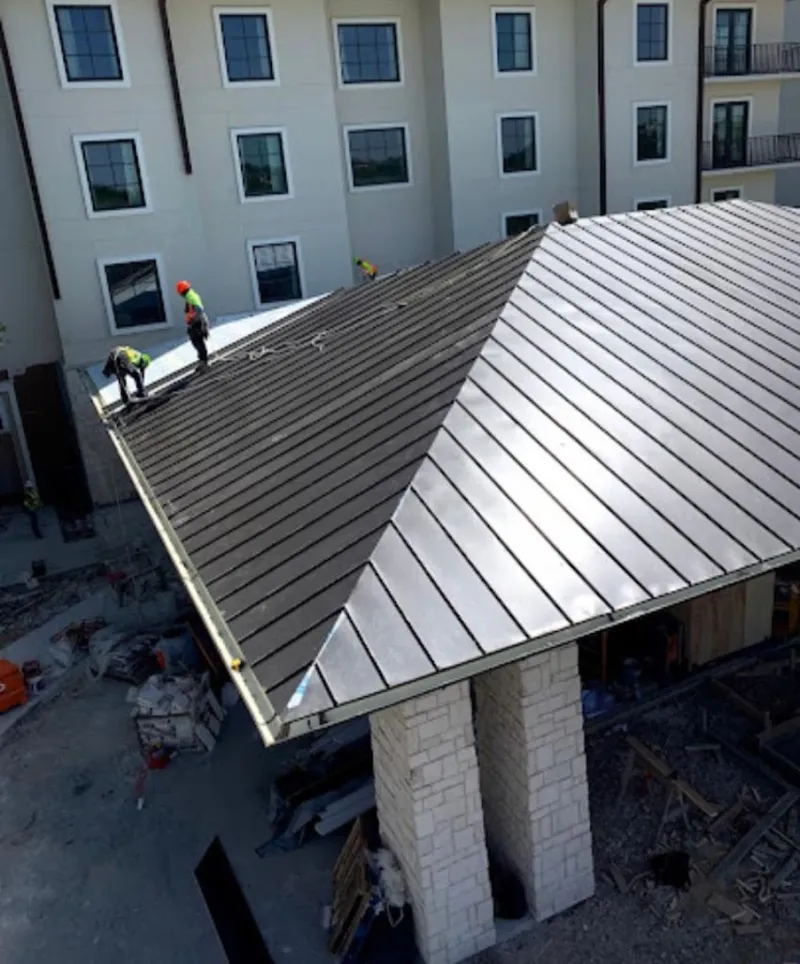 Crew installing standing seam metal roof panels on a commercial project in Coweta